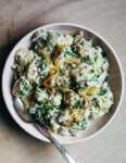 A bowl of herby potato salad with a serving spoon.