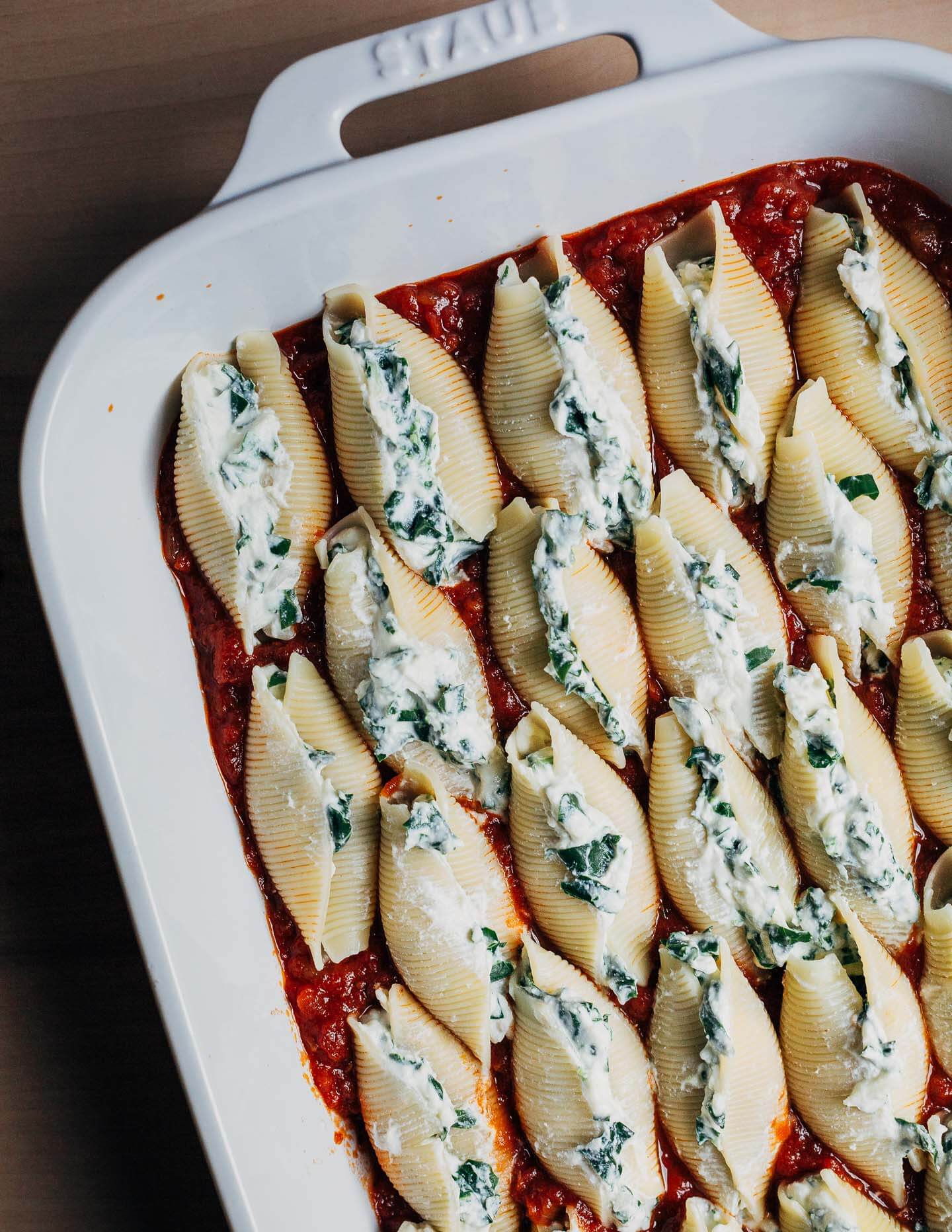 A baking dish with unbaked stuffed shells and marinara. 