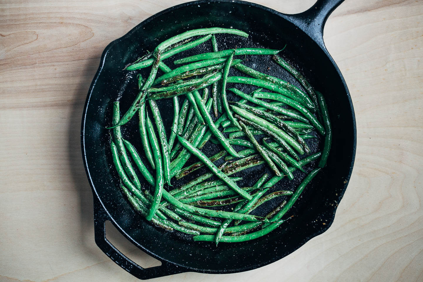 A cast iron skillet with vibrant green sautéed green beans. 