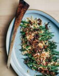 A platter of cooked green beans topped with golden breadcrumbs and fried shallots.