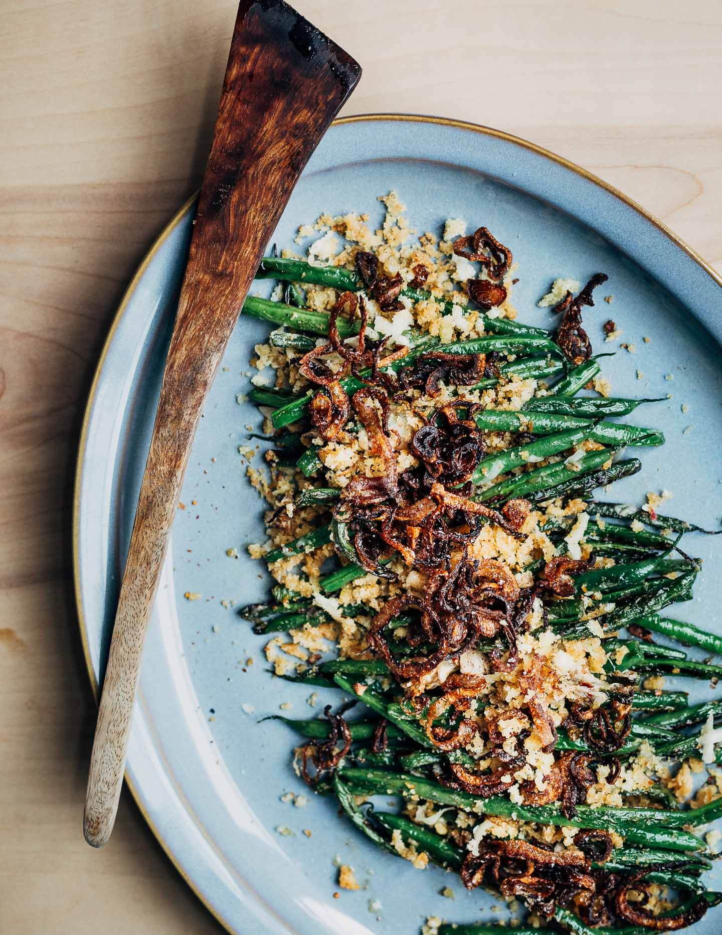 A platter of cooked green beans topped with golden breadcrumbs and fried shallots. 