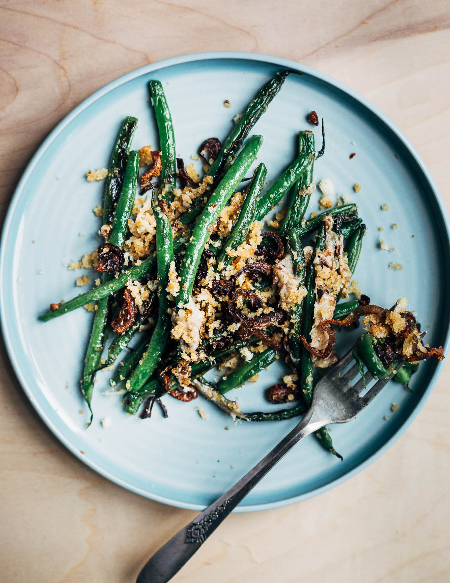 A plate with a serving of Parmesan green beans and a perfect bite arranged on a fork. 