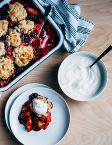 A dish of cobbler, with a serving on a plate and whipped cream alongside.