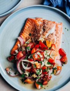 A piece of salmon on a plate topped with an herby tomato and fennel salad.