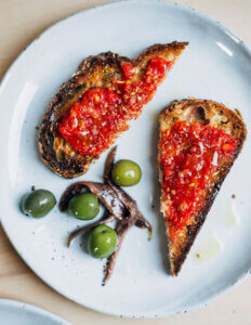 Two slices of pan con tomate on a plate with anchovies and olives.
