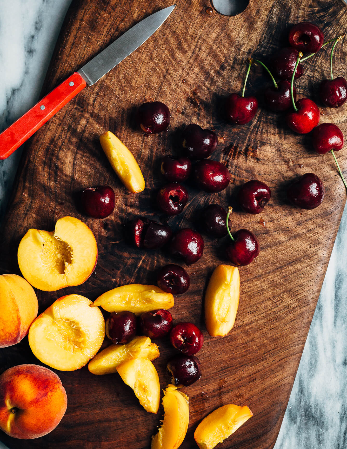 A cutting board with cherries, peaches, and a paring knife. 