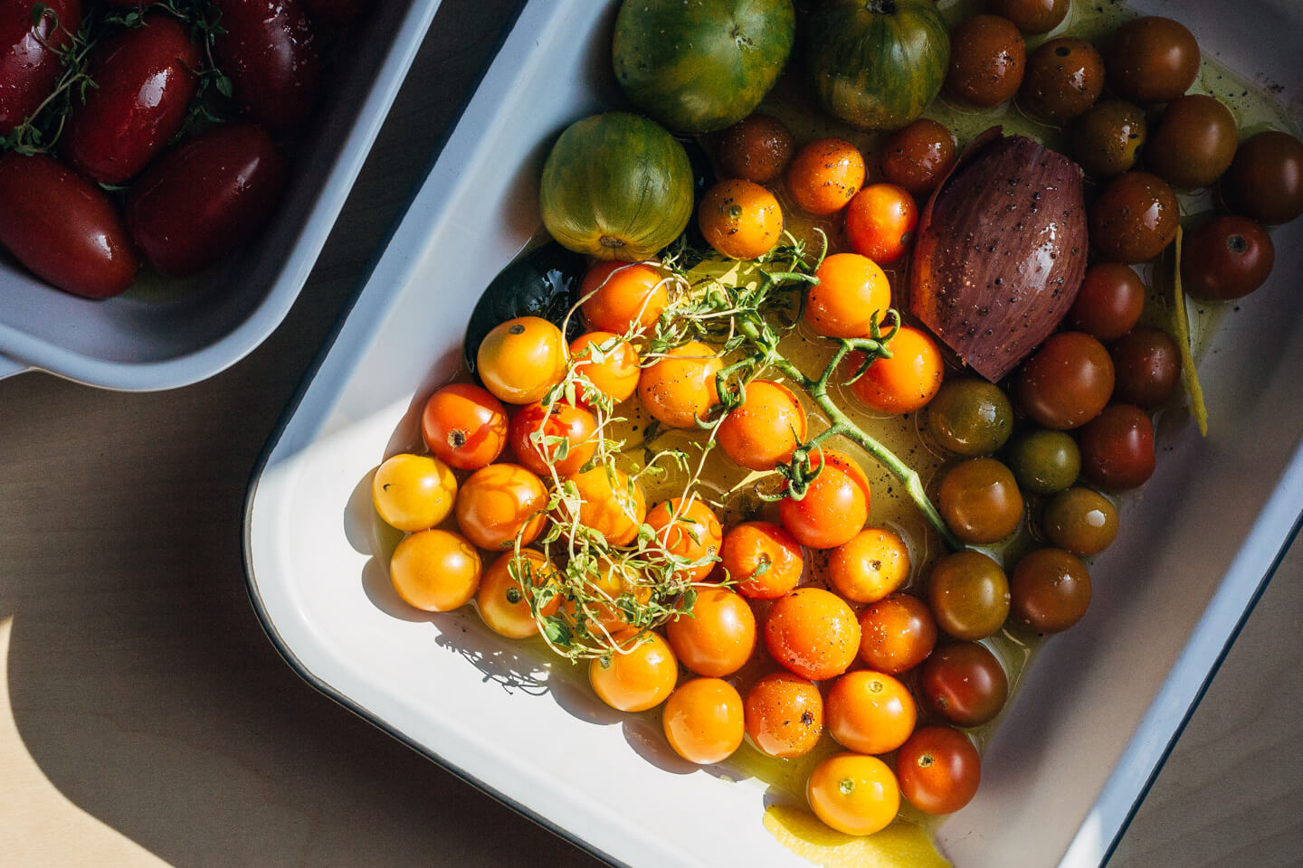 A baking dish with bright yellow cherry tomatoes, seen in raking sunlight. 