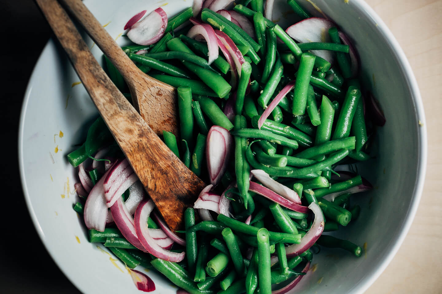 Green beans and pickled onions being tossed in a bowl. 