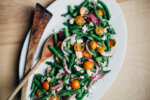 A white platter with green bean salad, with red onions, tomatoes, and feta.