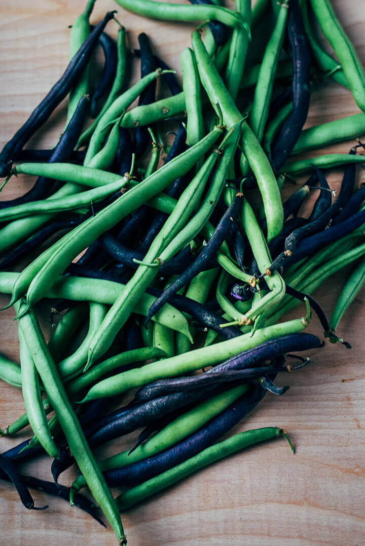 Green and purple green beans on a cutting board