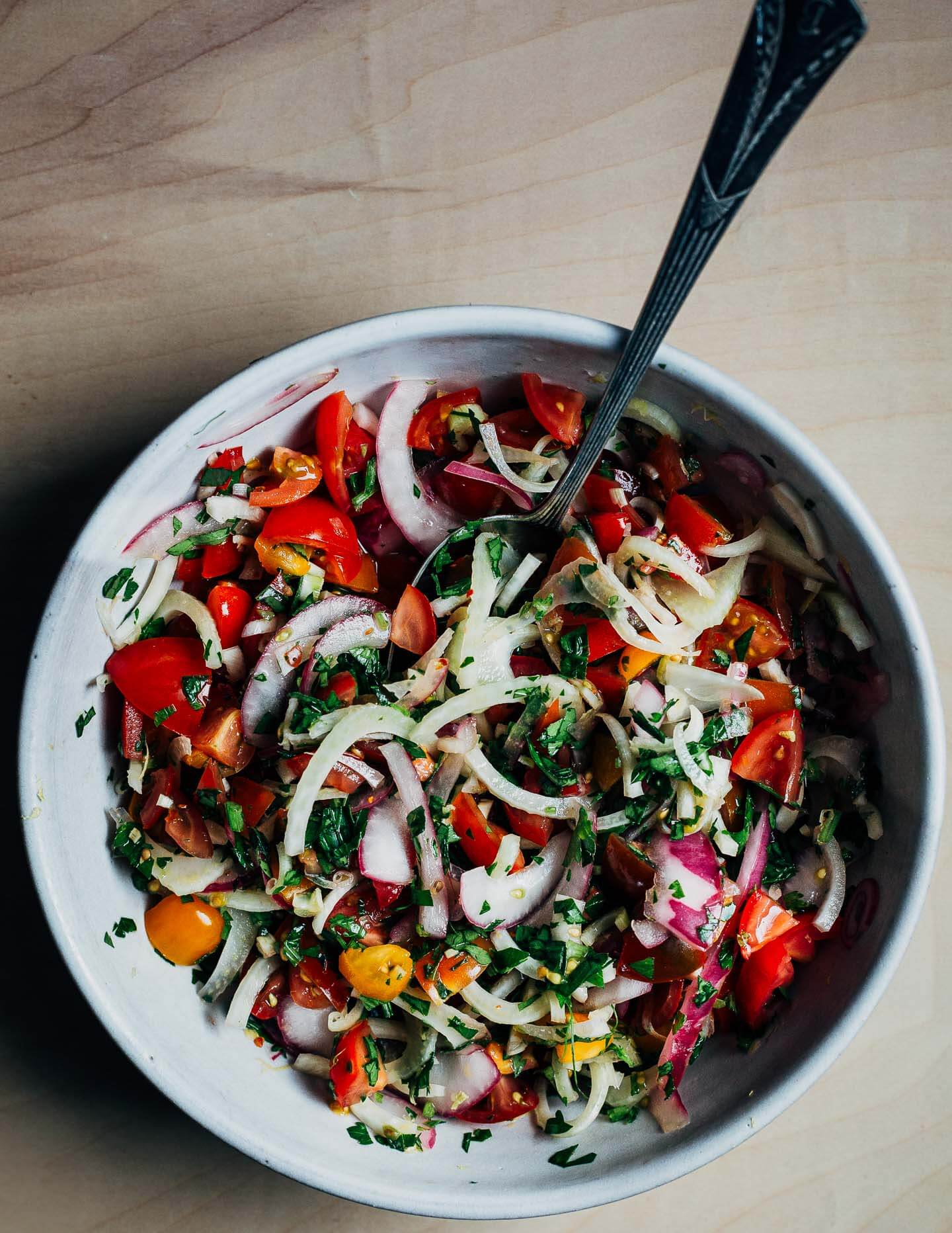 A bowl with tomato and fennel salad and a spoon.