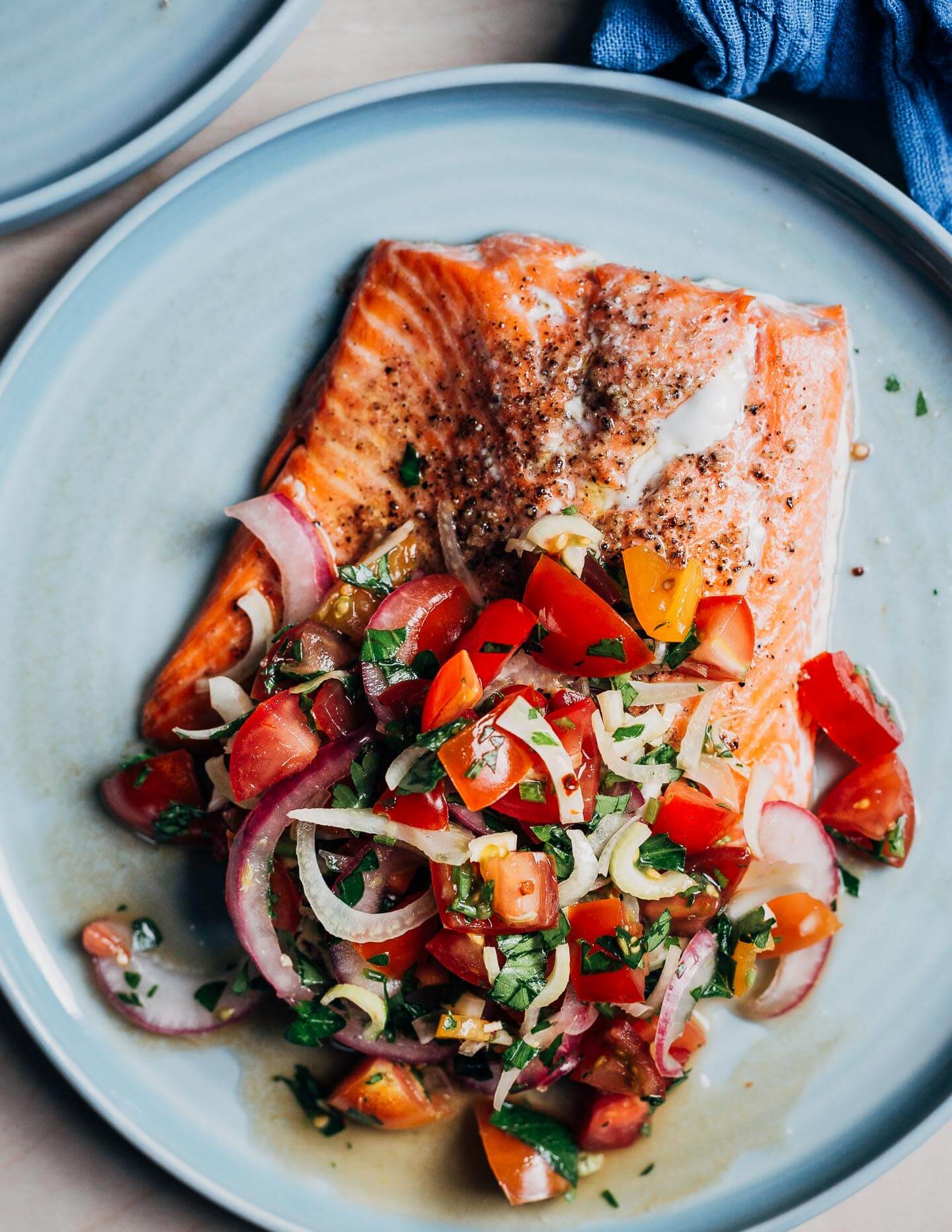 A salmon filet on a plate topped with a tomato and fennel salad.
