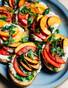 Toasts topped with ricotta, tomatoes, plums, and nectarines, arranged on a plate.