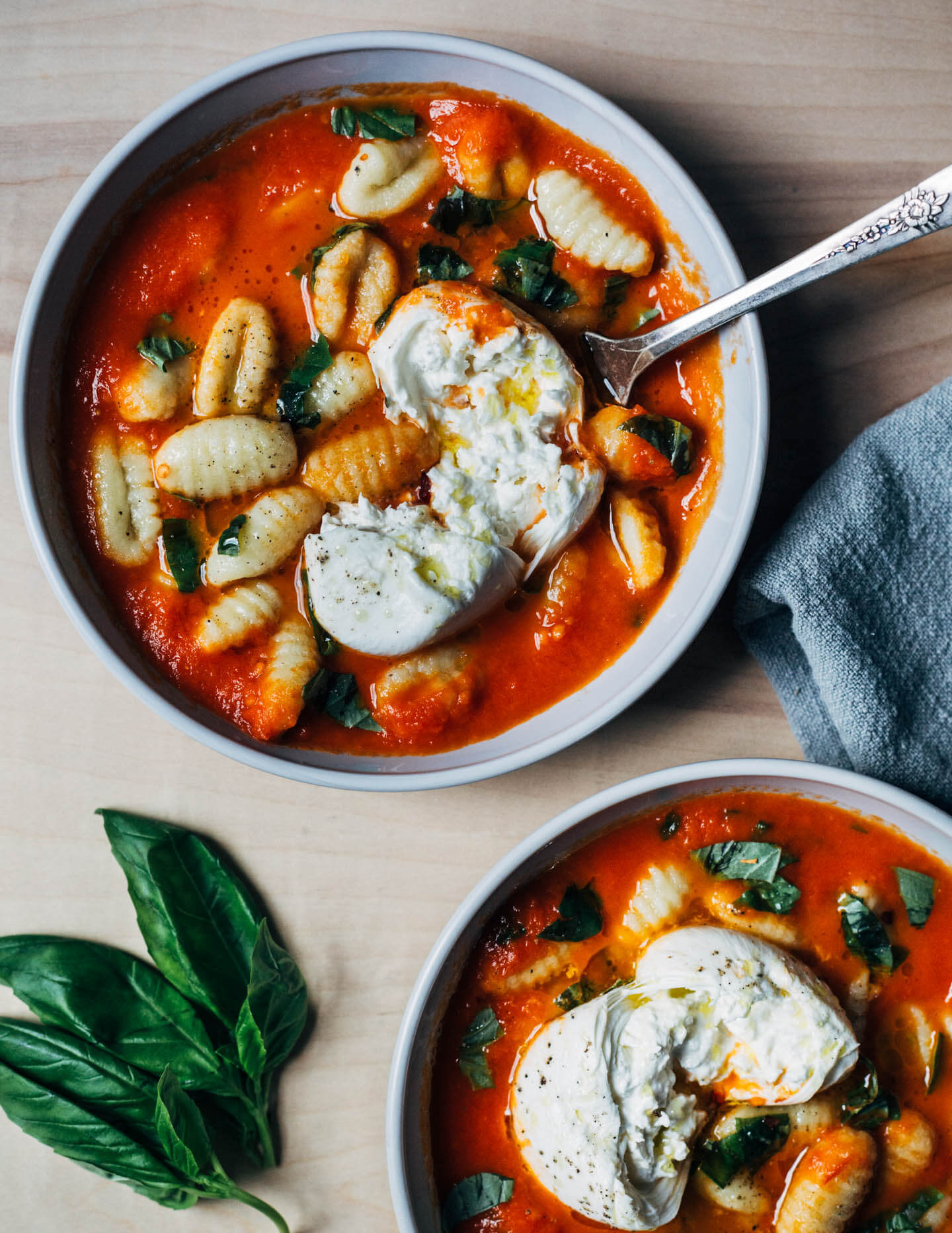 Two bowls with tomato sauce, gnocchi, burrata, and basil. 