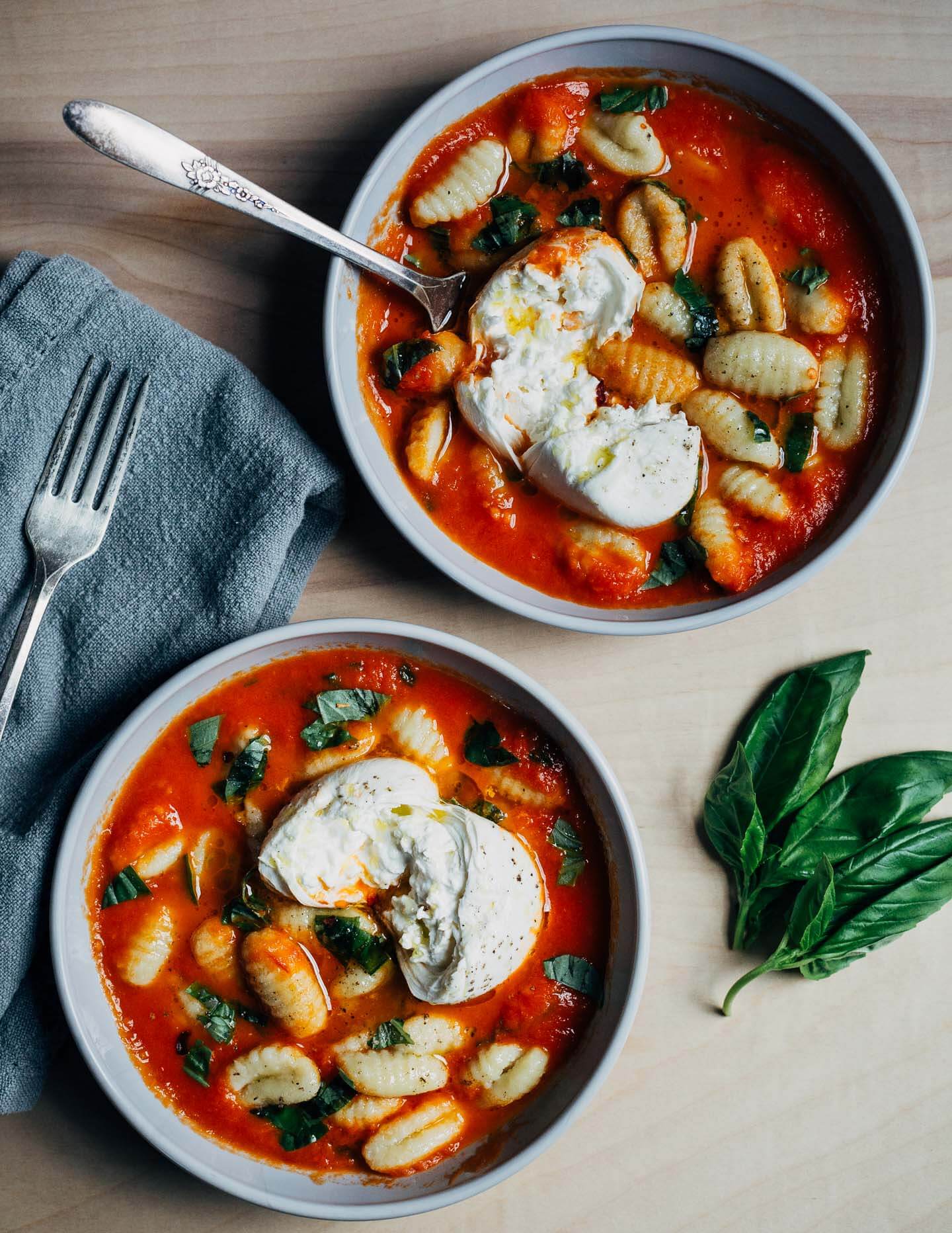Two bowls with tomato sauce, gnocchi, burrata, and basil.