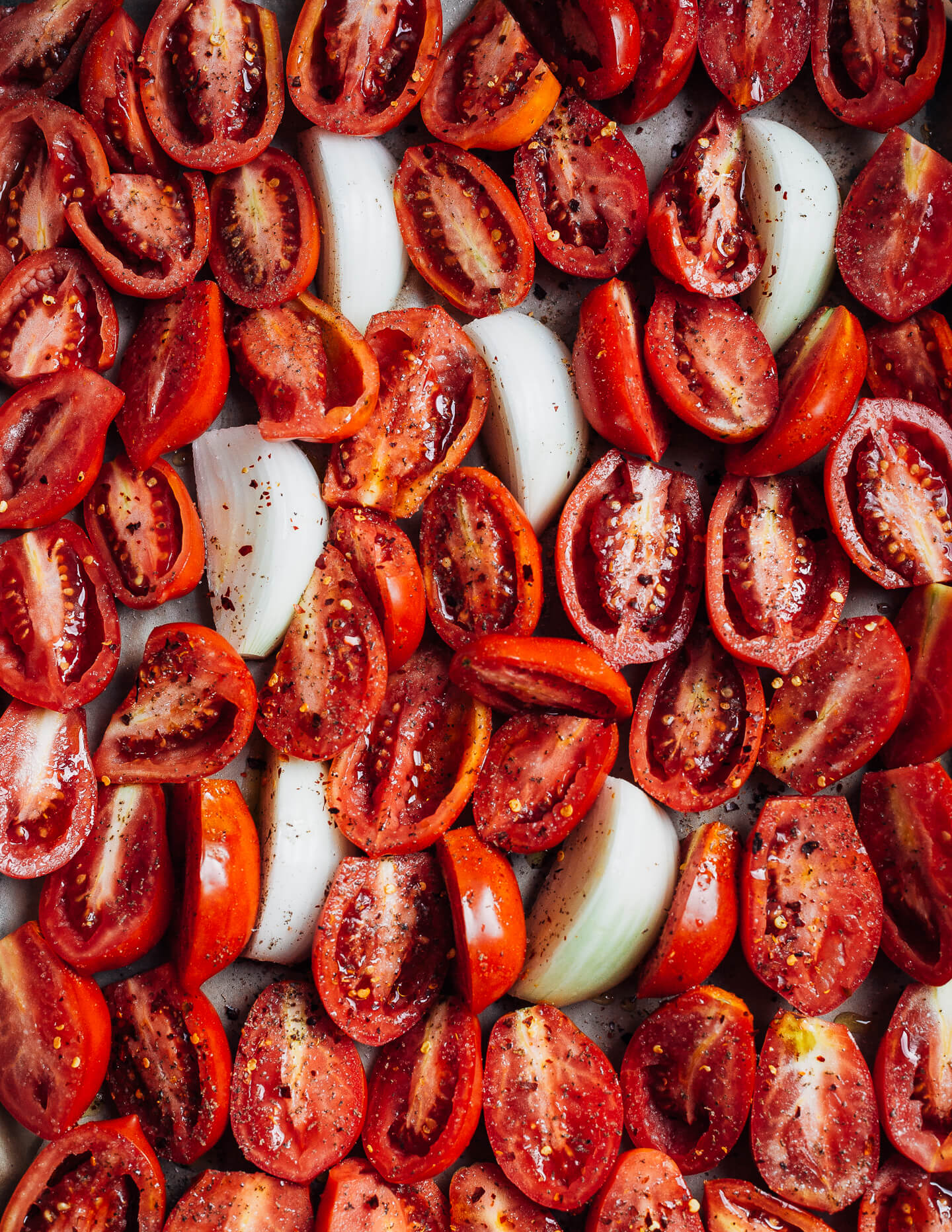 A sheet pan with halved tomatoes and onions. 
