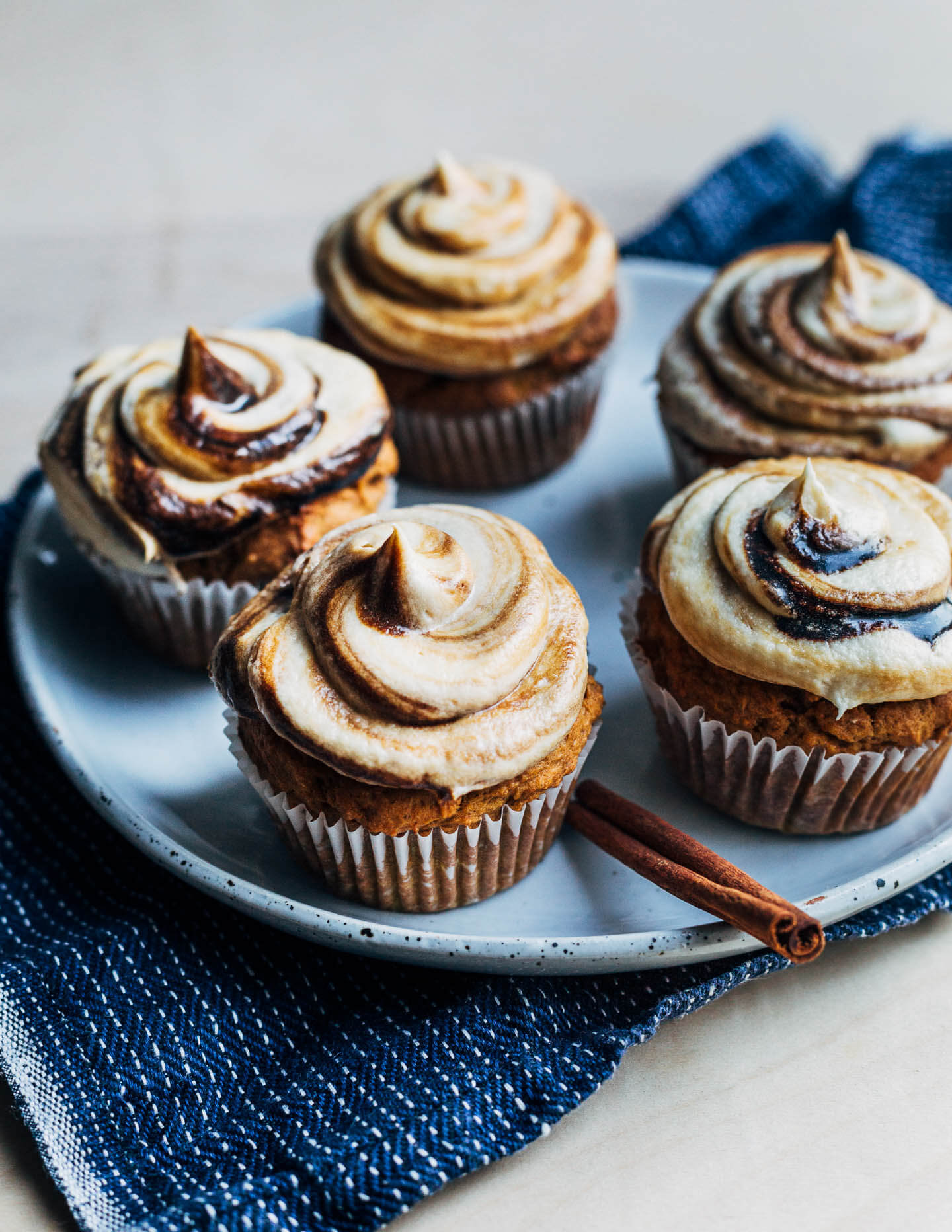 Frosted cupcakes on a plate with a stick of cinnamon. 