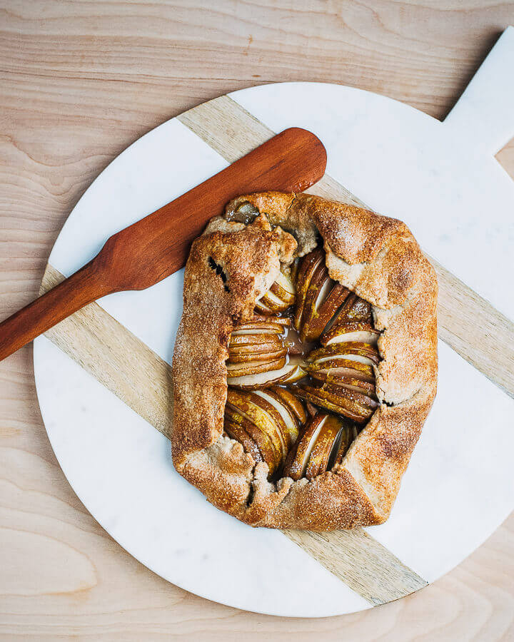 A pear galette on a marble slab with a wooden server alongside. 