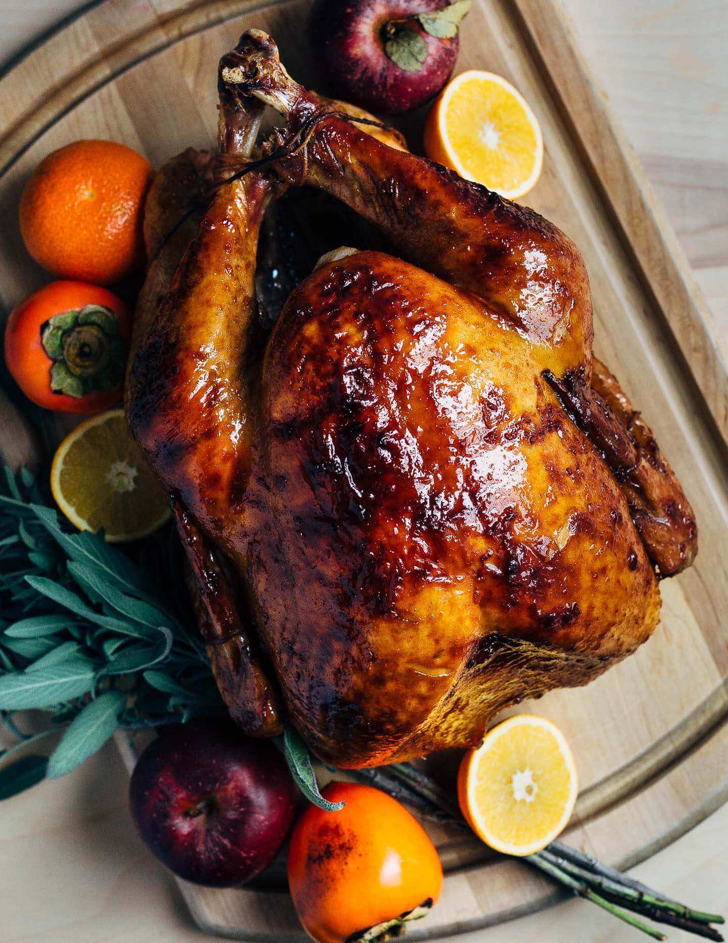 A deep-golden glazed turkey on a platter with fruit and herbs. 