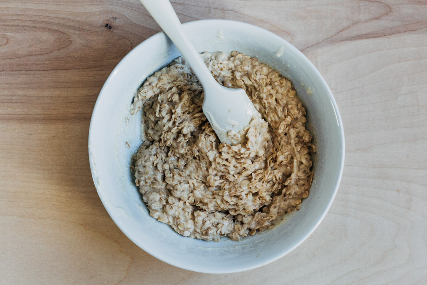 A bowl of oatmeal lace cookie batter with a silicone spatula. 