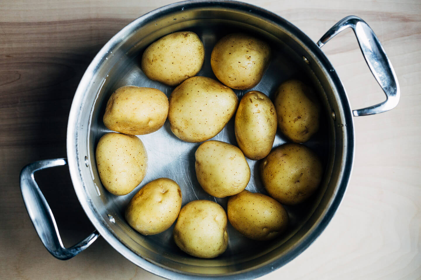 A pot with whole potatoes covered in water.