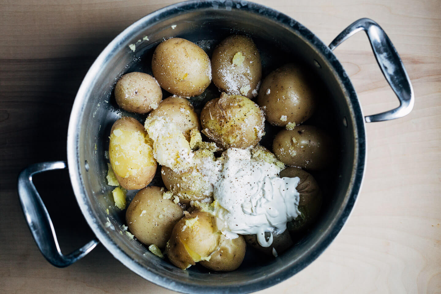 Cooked potatoes in a pot with a big dollop of sour cream and salt sprinkled on top.