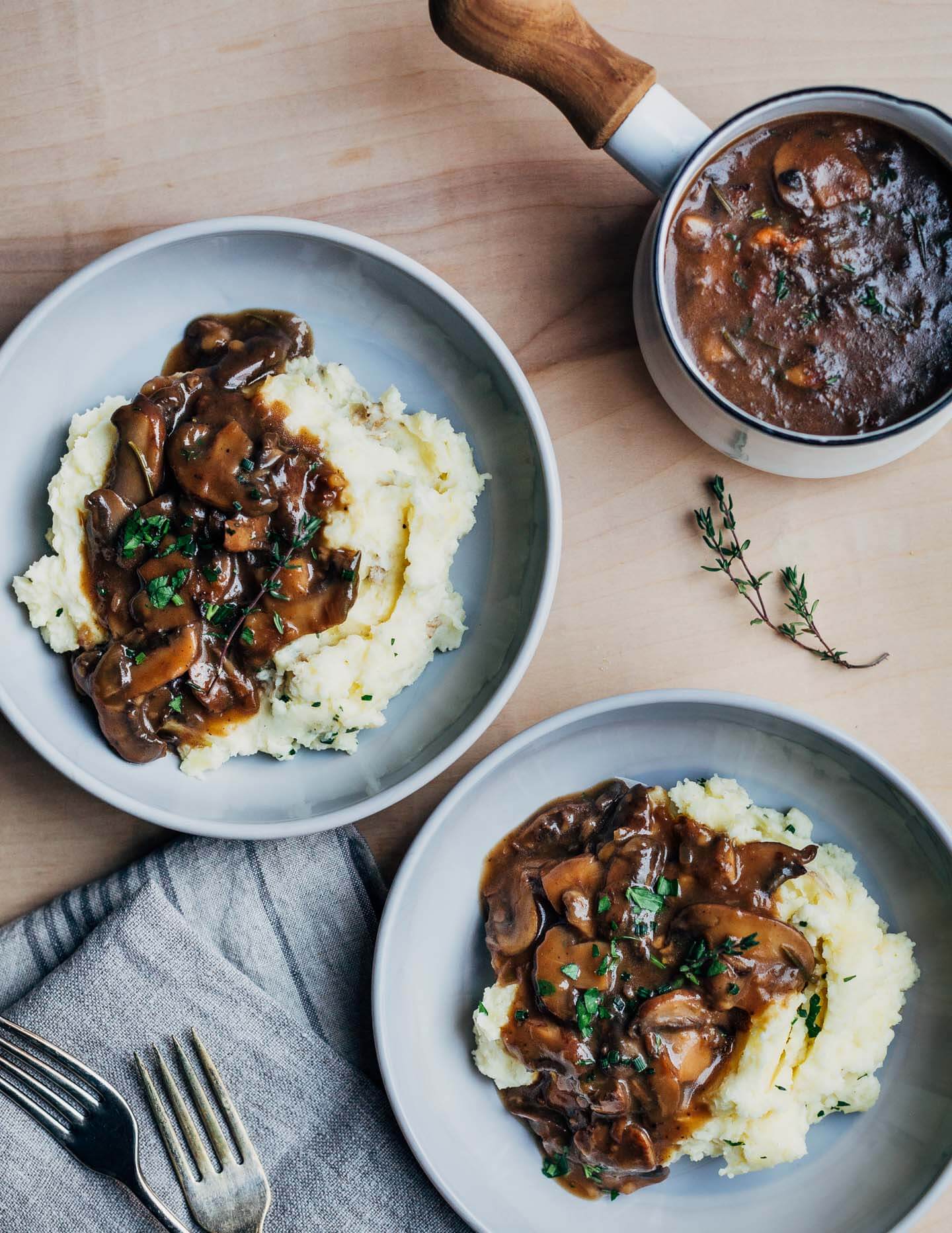 Two bowls of mashed potatoes and gravy, with a gravy boat alongside. 