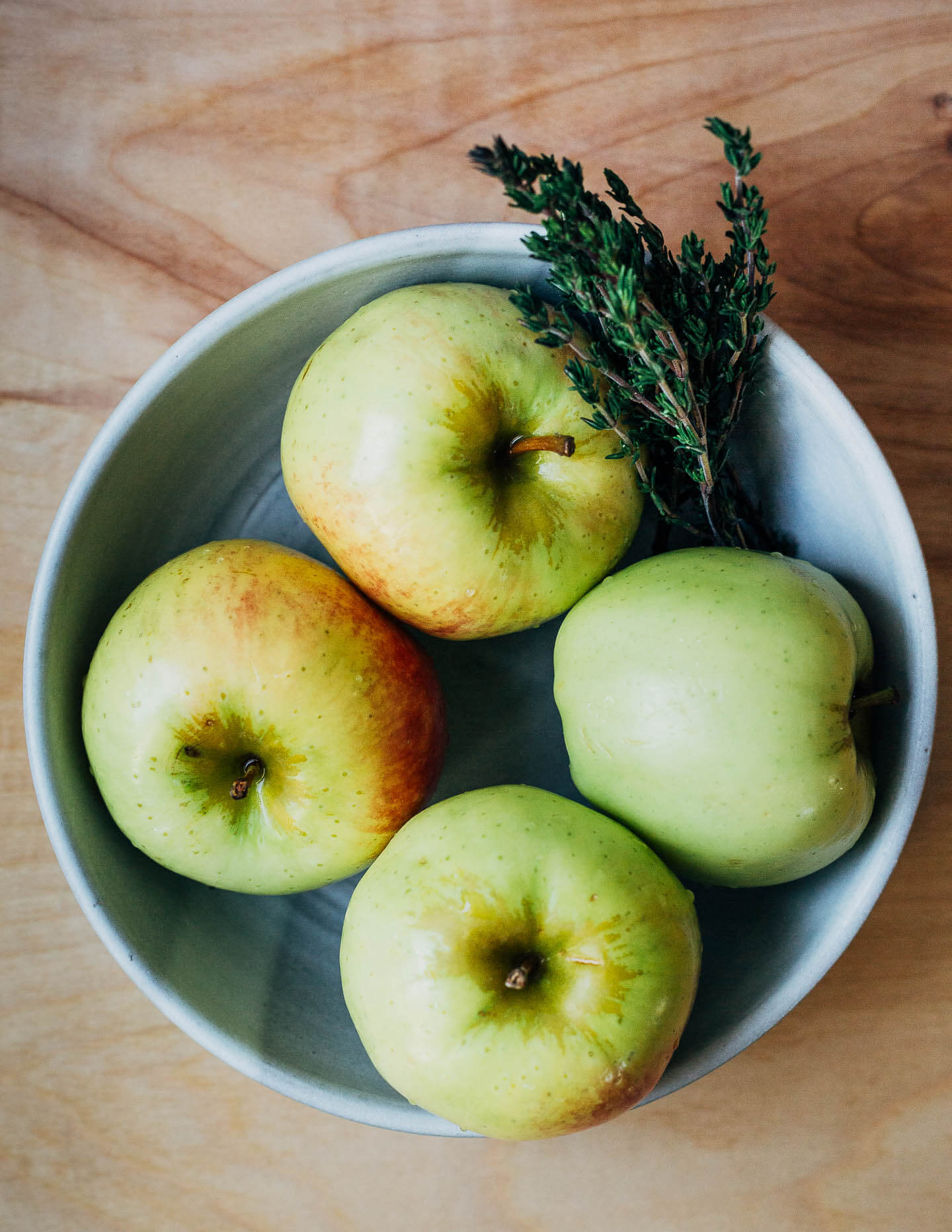 A bowl of green apples with sprigs of fresh thyme. 