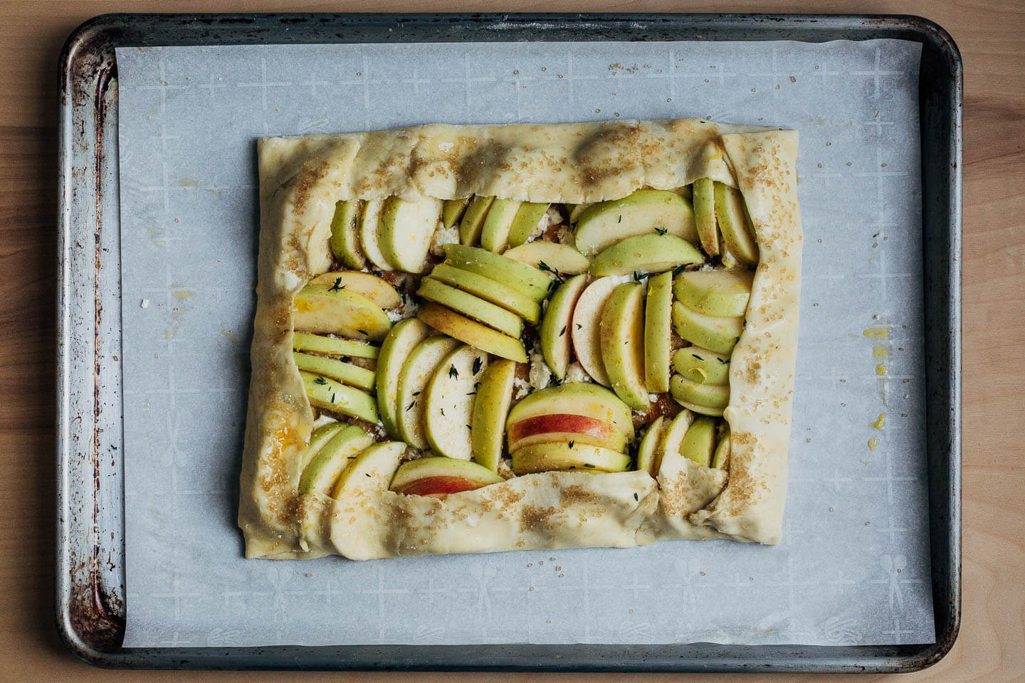 A crimped up apple tart on a baking sheet, ready to bake. 