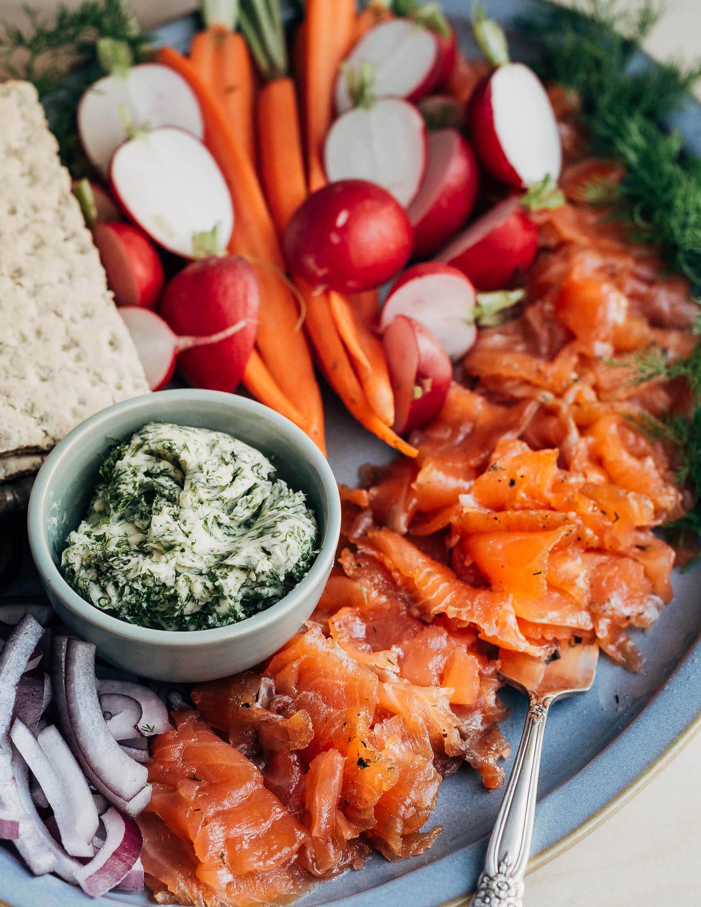 A platter of gravlax with crackers, carrots, radishes, and red onions. 