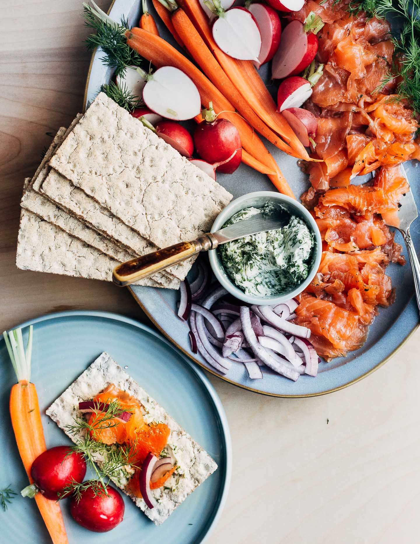 A platter of gravlax with crackers, carrots, radishes, and red onions, with a little serving plate alongside. 