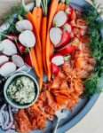 A platter of gravlax with crackers, carrots, radishes, and red onions.