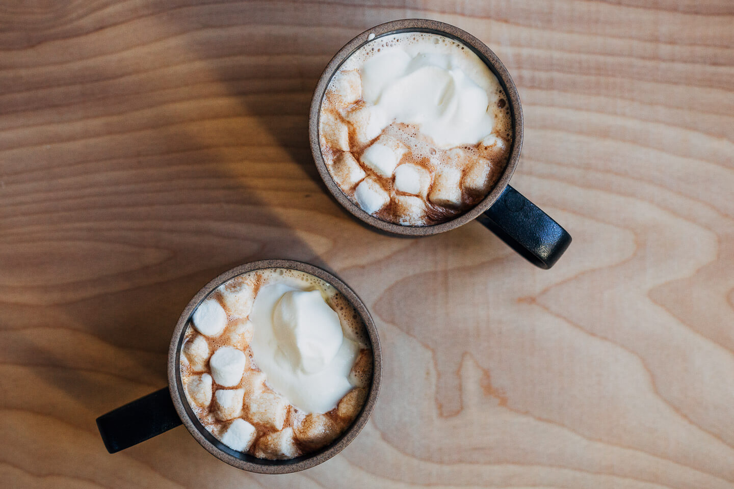 Two mugs of hot chocolate on a plain table. 