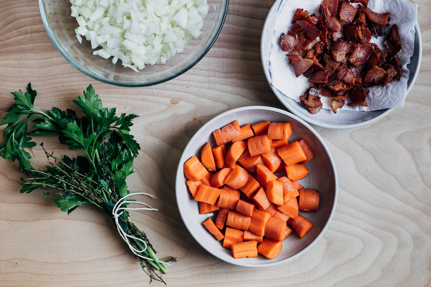 Mise en place: bowls of diced onions, cooked lardons, and chopped carrots, and a bouquet garnis