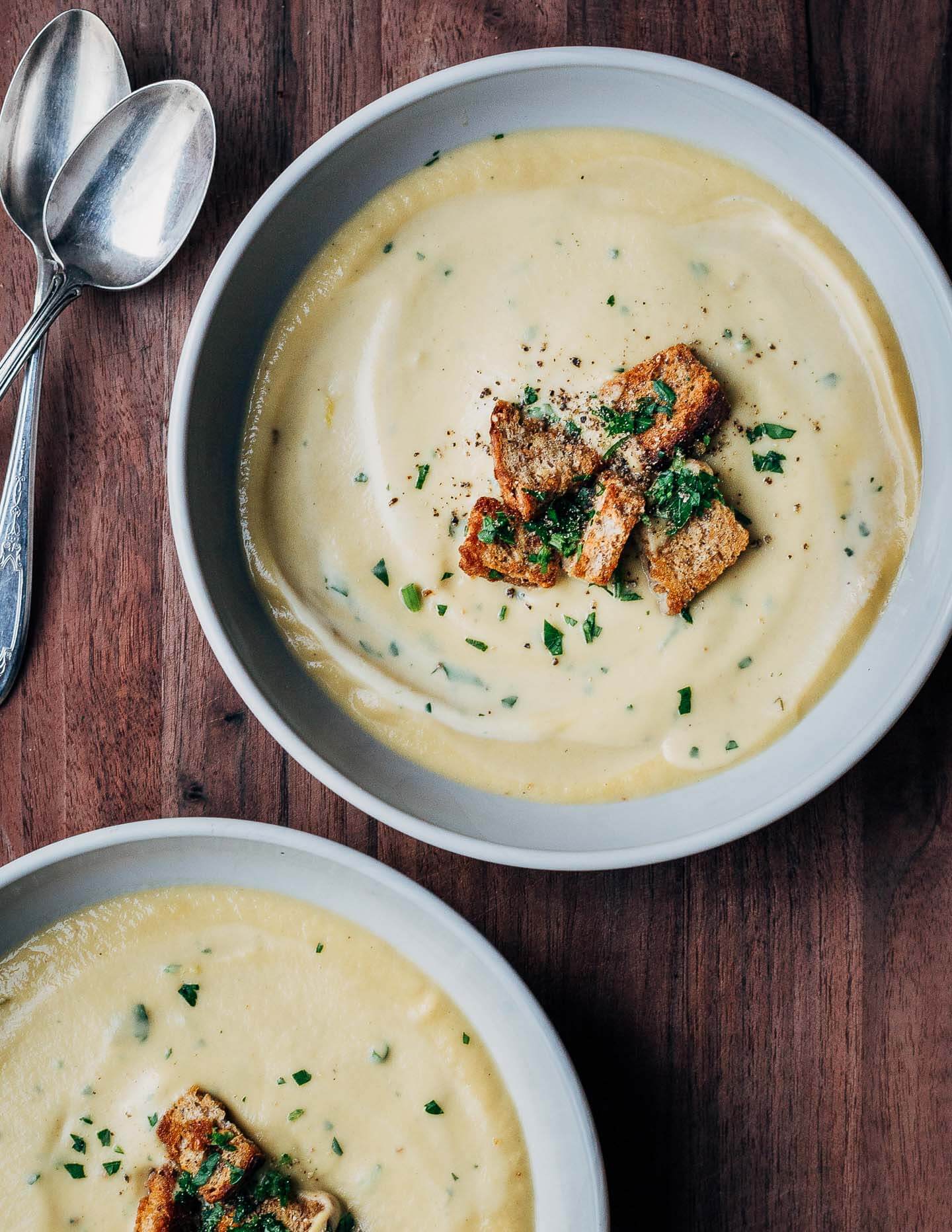 Two bowls of celery root soup topped with herbs and croutons.