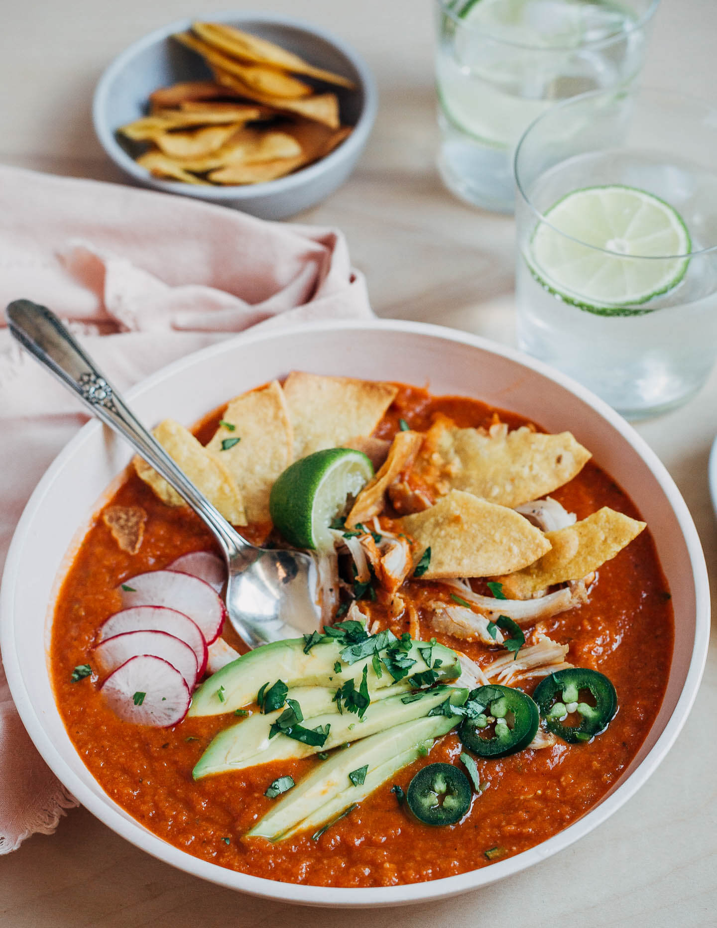 A bowl of tortilla soup topped with avocado, radishes, jalapeños, fried tortillas and chicken.