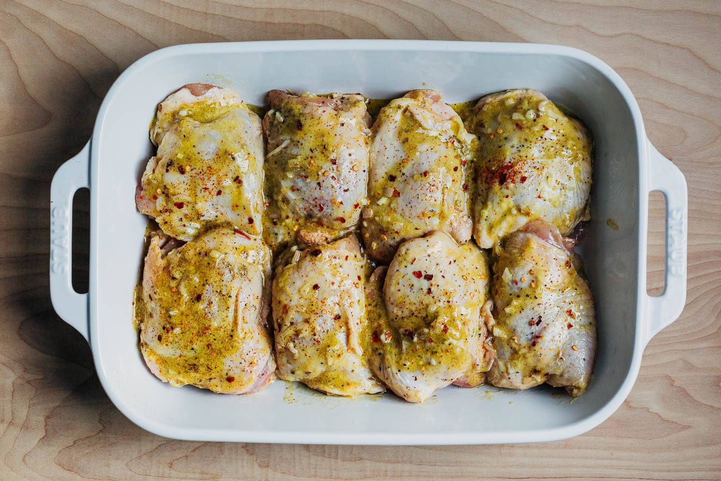 Marinating raw chicken thighs in a baking dish. 