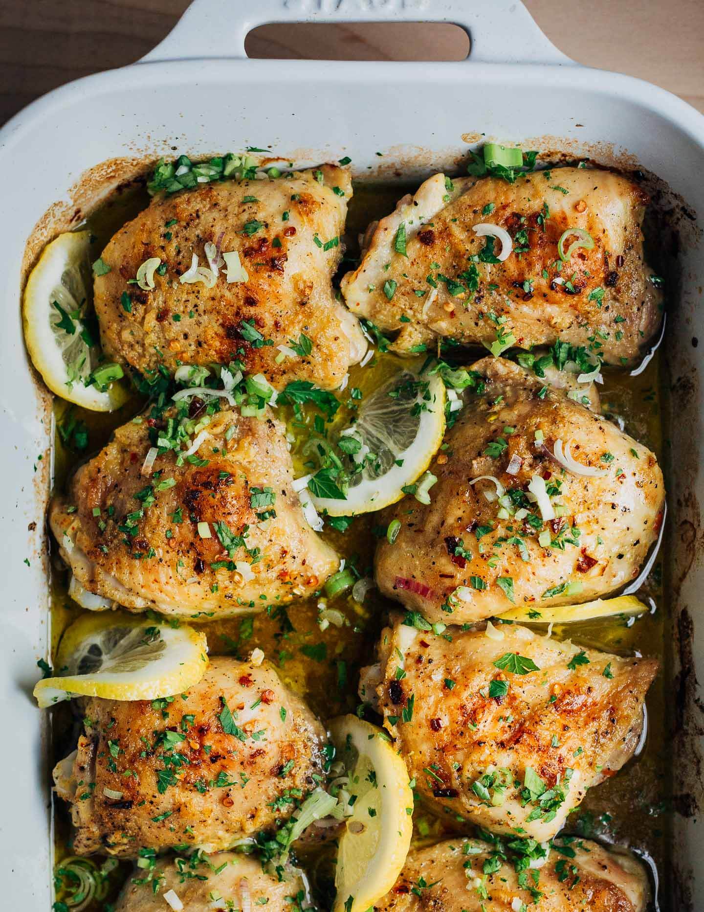 Baked chicken thighs with lemon slices and herbs in a baking dish. 