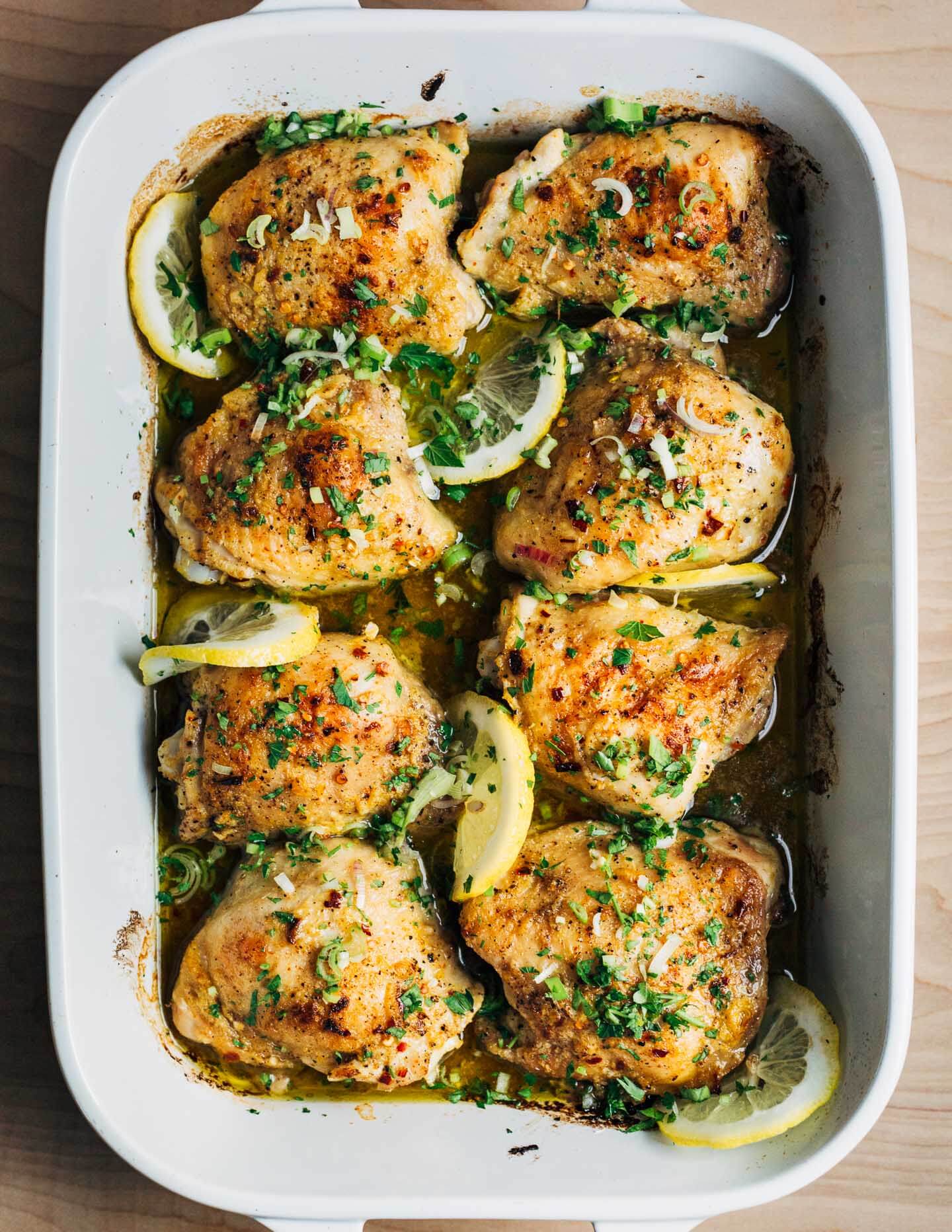A baking dish with baked chicken thighs with lemon and herbs. 
