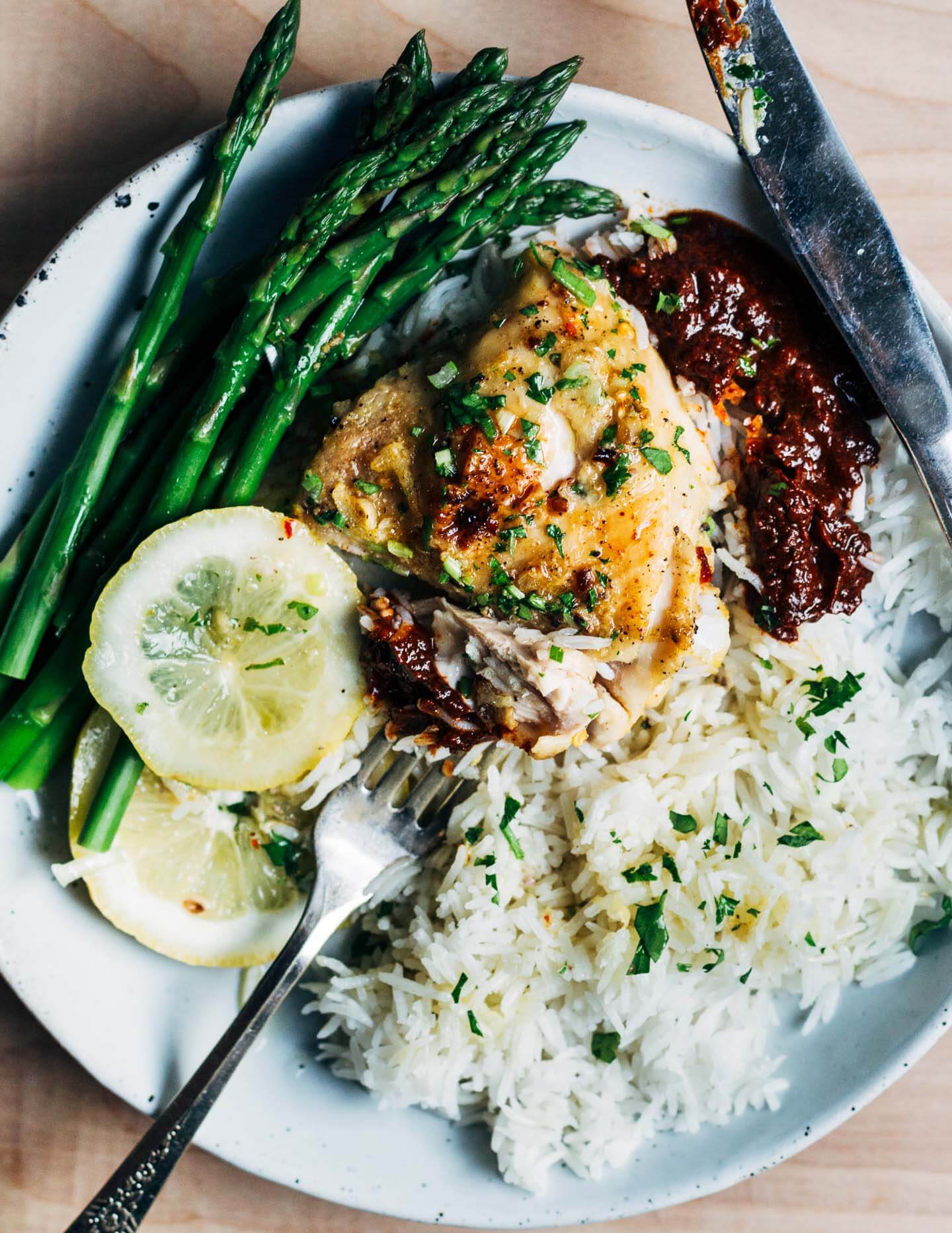 A plate with a bite of chicken on a fork with ice, harissa, and asparagus