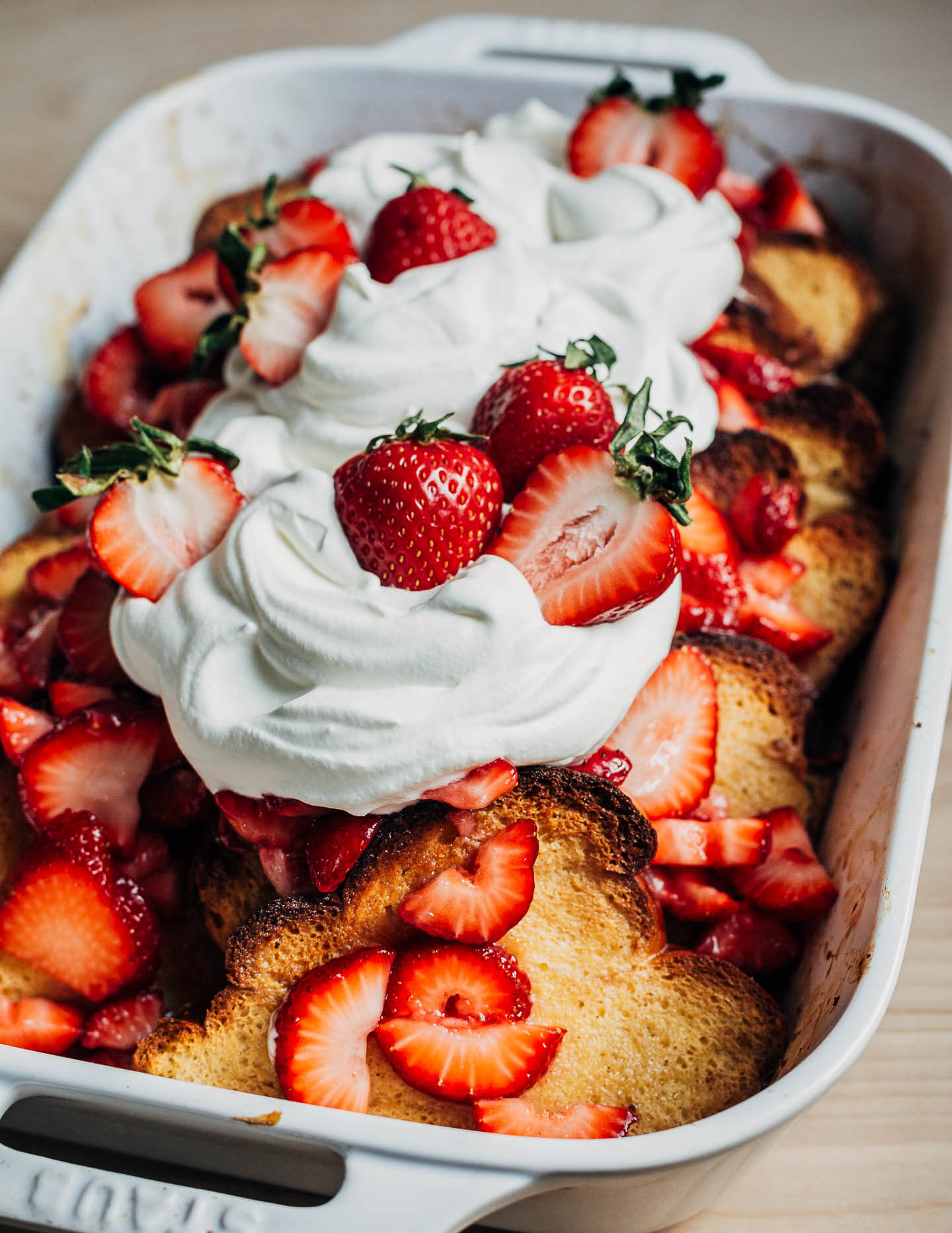 A baking dish with baked French toast topped with whipped cream and strawberries.