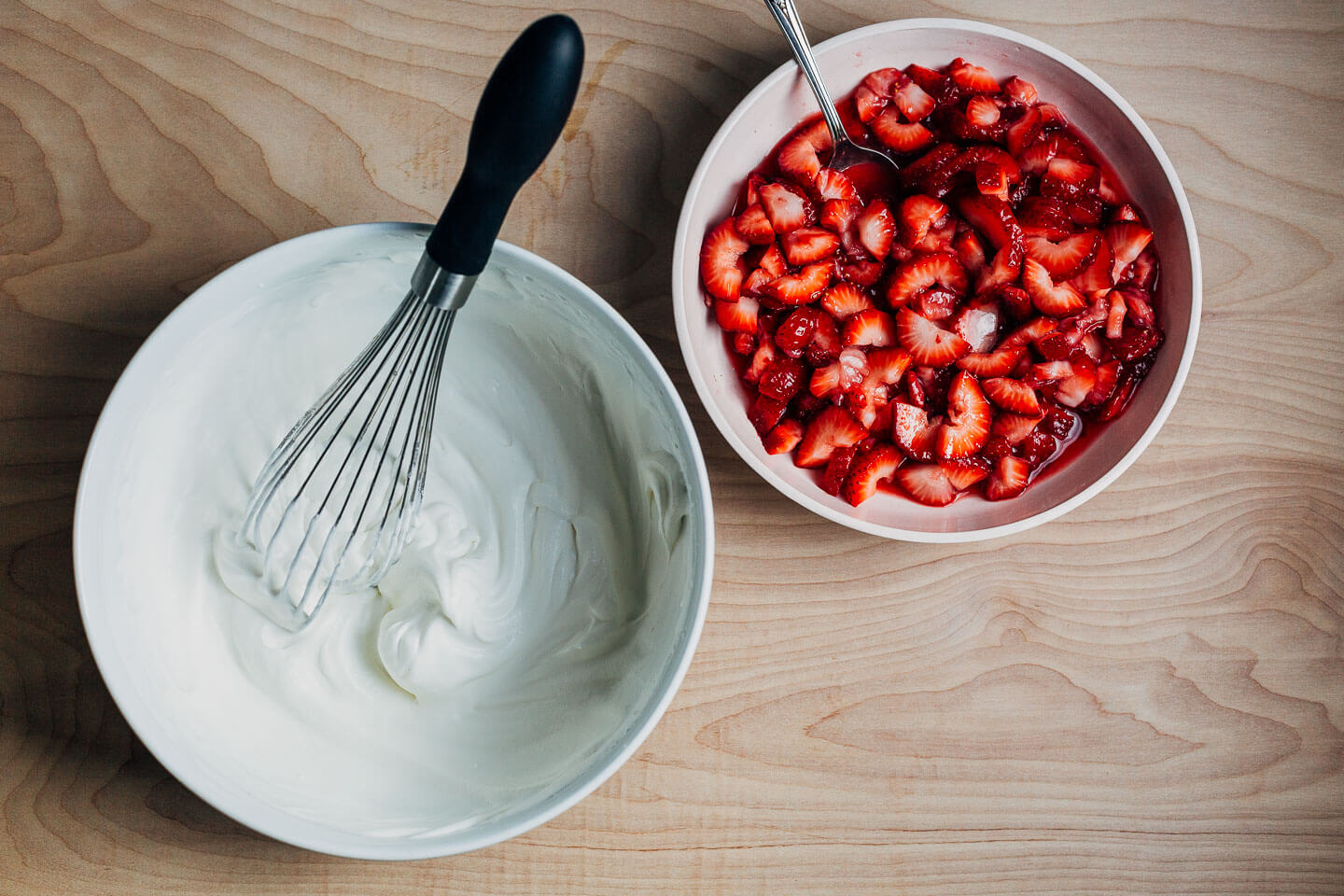 A bowl of whipped cream alongside a bowl of strawberries