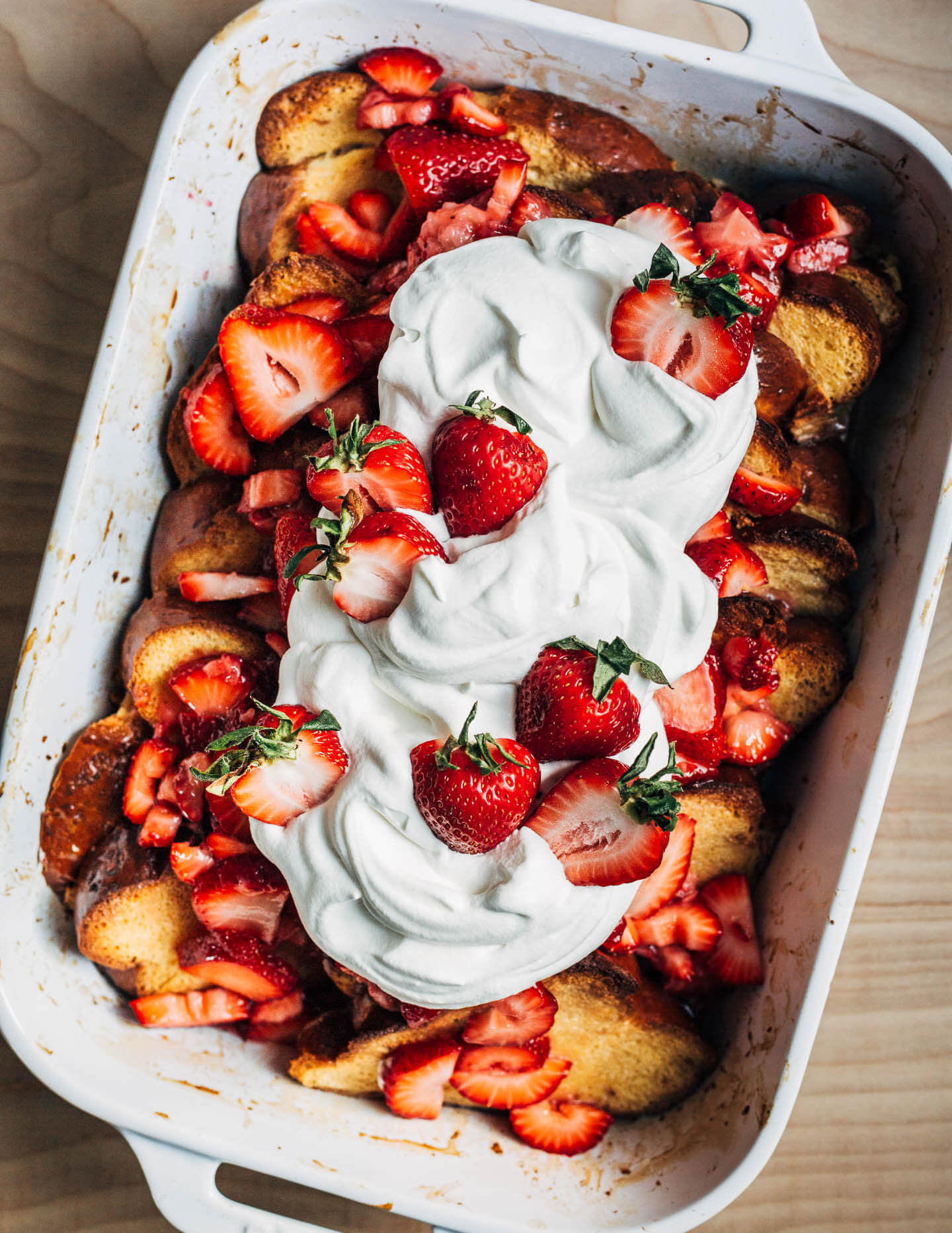 A baking dish with baked French toast topped with whipped cream and strawberries.
