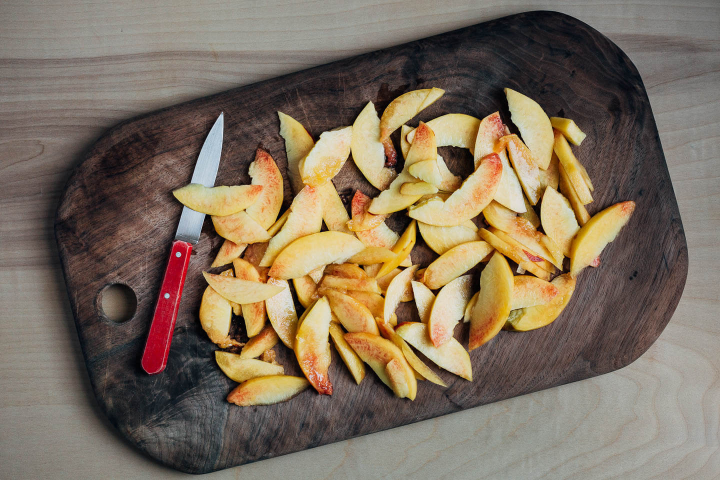 Sliced peaches on a dark wood cutting board