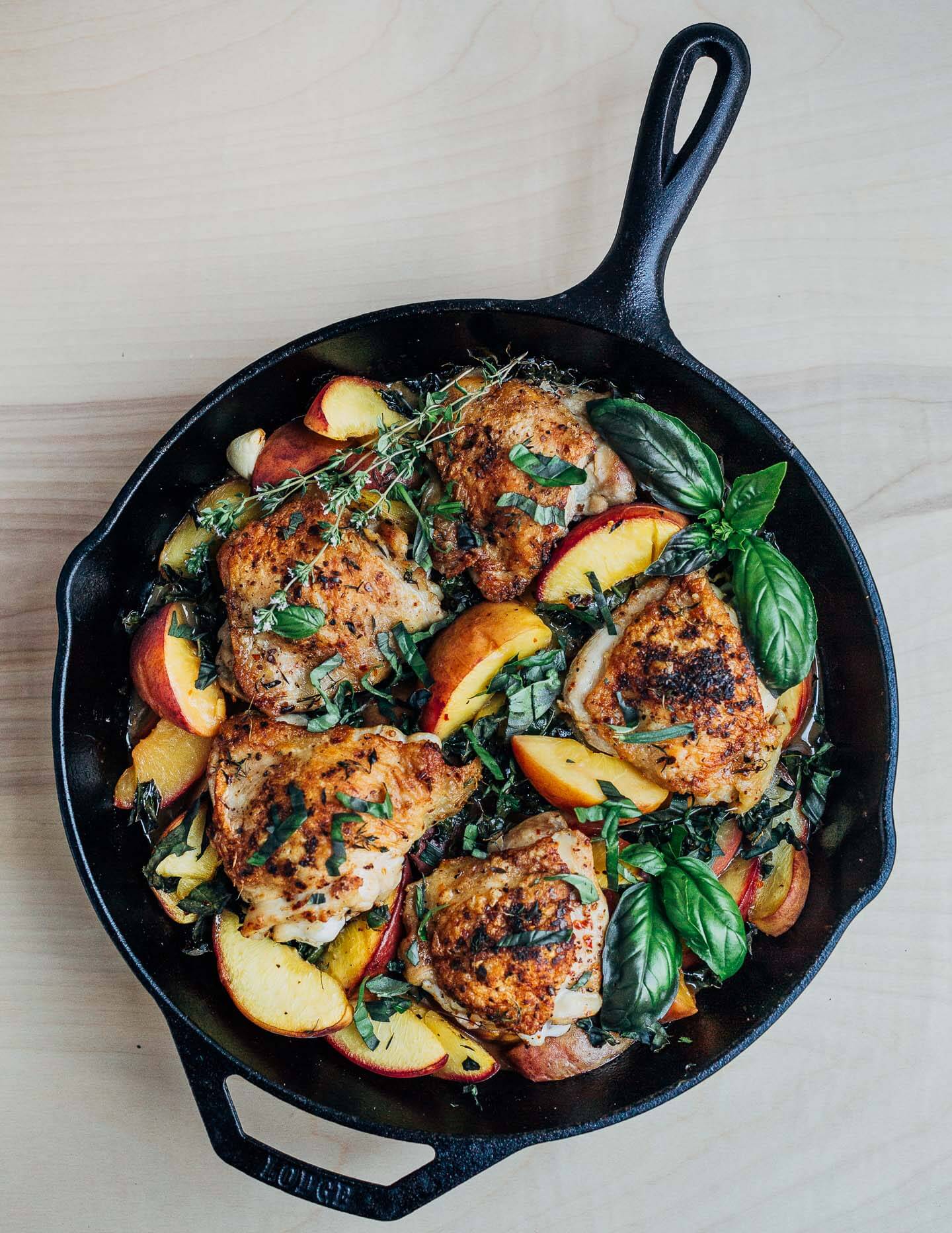 A skillet with golden chicken, peaches, and herbs.