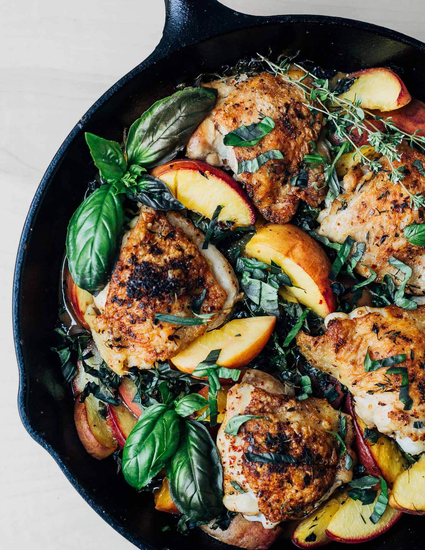 A skillet with golden chicken, peaches, and herbs. 
