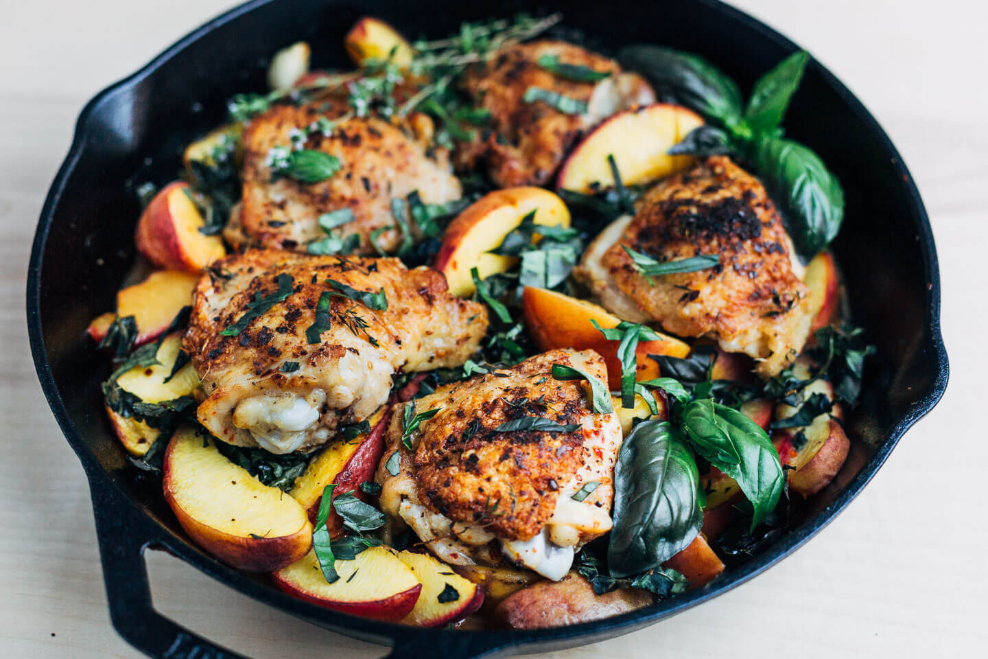 Side view of a skillet with chicken and peaches