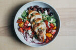 A wide bowl with a Greek salad topped with sliced chicken breasts.